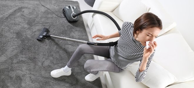 Mujer estornudando en un sofá mientras aspira su alfombra