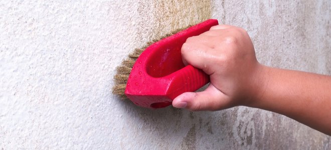 Mano pequeña limpieza de pared blanca sucia con cepillo