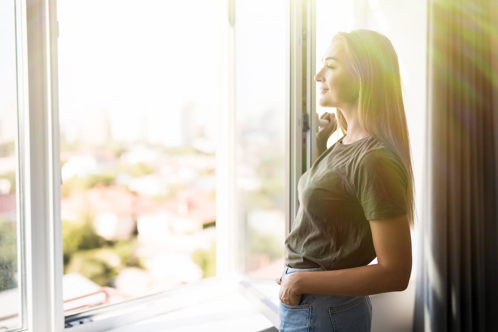 Mujer de pie junto a la ventana abierta con luz entrando