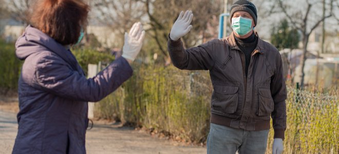 dos personas que se saludan mientras se alejan socialmente con máscaras