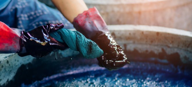 Manos enguantadas exprimiendo el tinte azul de la tela