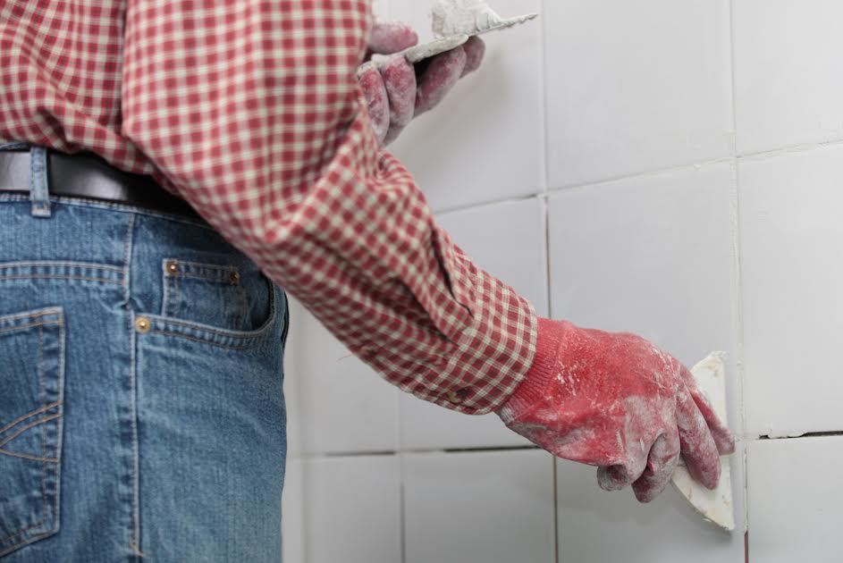 Un hombre aplicando lechada en una pared de ducha de azulejos. 