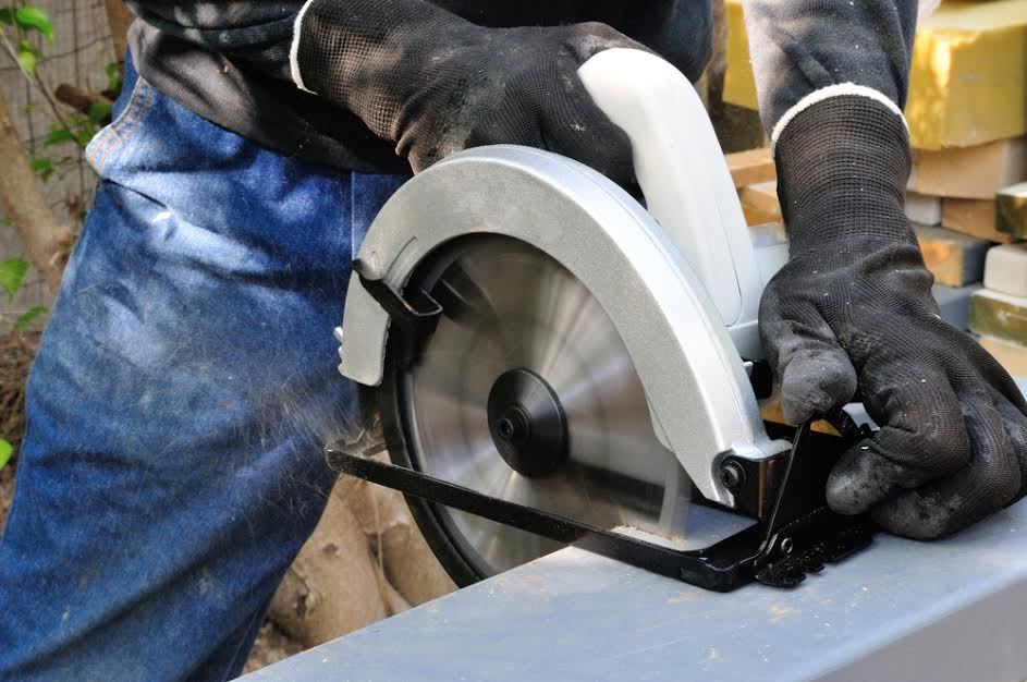 Alguien con guantes de trabajo usando una sierra afuera.