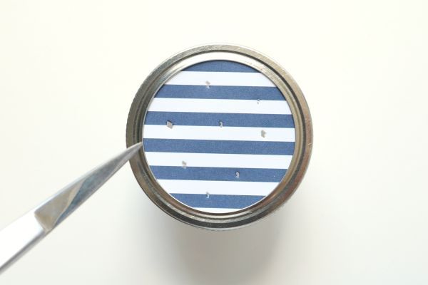 Un par de tijeras que hacen agujeros en la tapa de papel de un frasco de conservas.