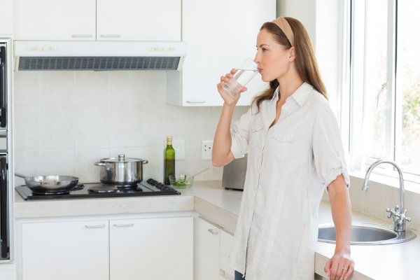 Una mujer de pie en una cocina bebiendo un vaso de agua. 