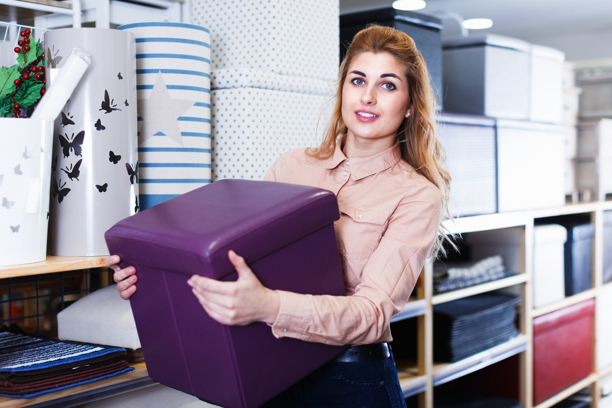 Una mujer sostiene un ottomon de almacenamiento púrpura. 
