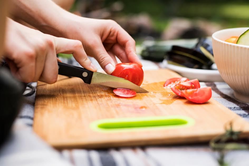 Alguien cortando un tomate en una tabla de cortar afuera. 