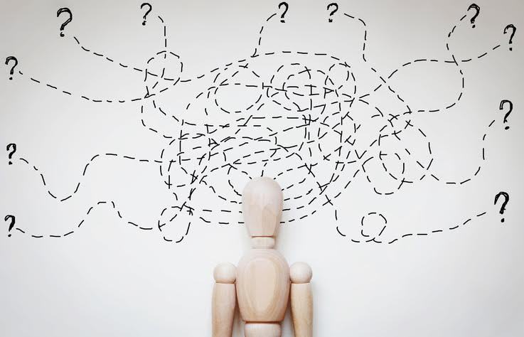 Un hombre de madera con líneas de pensamiento y signos de interrogación en un lío enredado. 