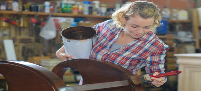 Una mujer manchando un cobertizo de madera en un taller. 