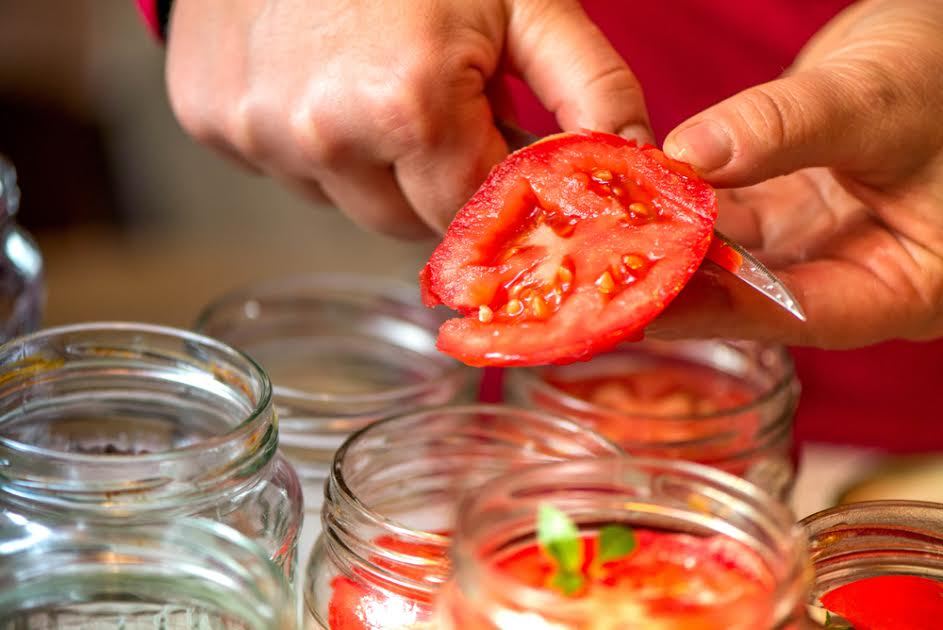 Cortar tomates en frascos para conservas.