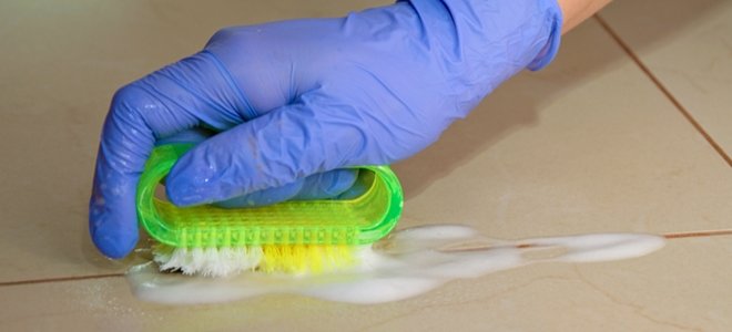 una lechada de limpieza a mano enguantada entre las baldosas con un cepillo