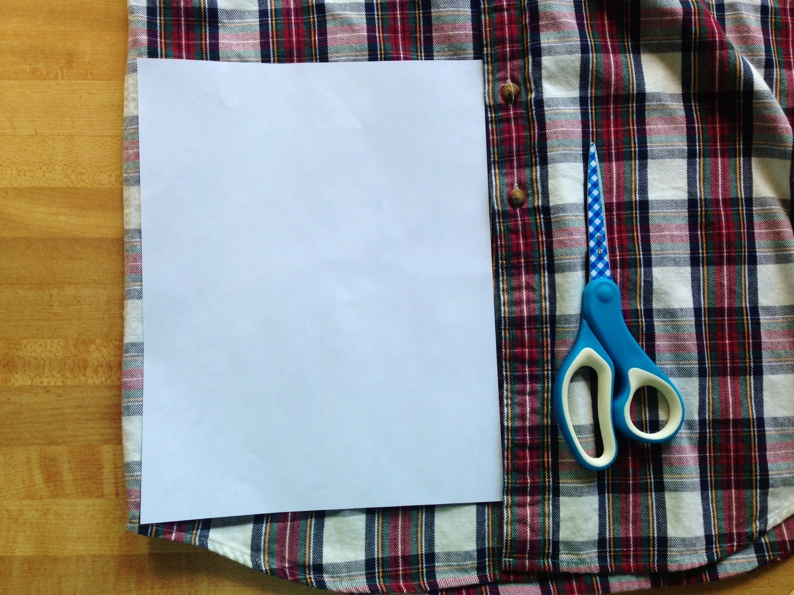 Papel sobre una camisa a cuadros con unas tijeras. 