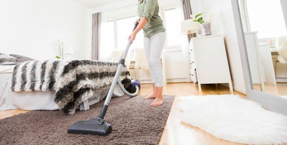 Una mujer aspirando una alfombra en una habitación blanca y limpia.