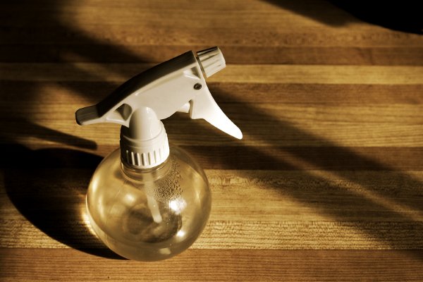 Una botella de spray sentada sobre una mesa de madera con sombras. 