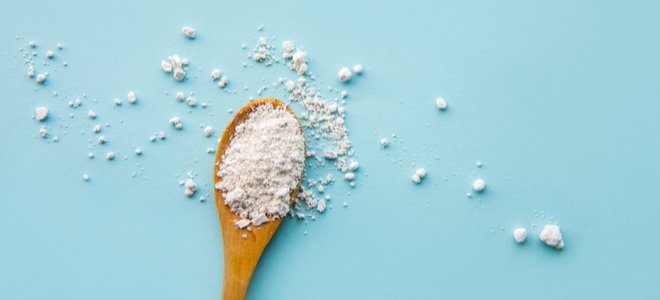 Polvo blanco en cuchara de madera sobre fondo azul.