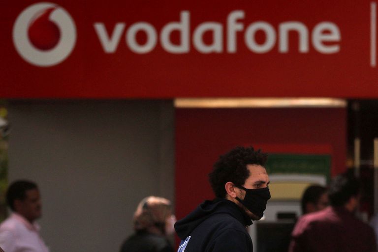 Un hombre camina ante un cartel de Vodafone.