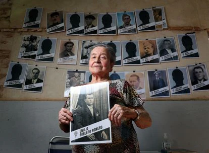Regina Robledo muestra una fotografía de su padre, Emilio, frente al mural de retratos de las víctimas que preside la entrada a la fosa común donde fueron enterrados. 