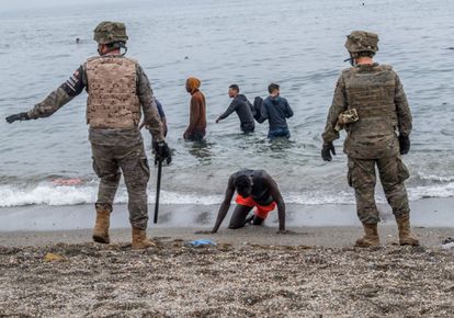 Un hombre arrodillado en una playa de Ceuta mientras el Ejército acordona la zona, el pasado martes.