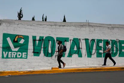 Dos personas caminan delante de una pintada del Partido Verde, en Ciudad de México, en junio.