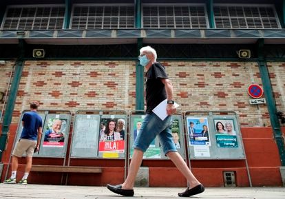 Un hombre camina en San Juan de Luz delante de carteles de las elecciones regionales francesas.