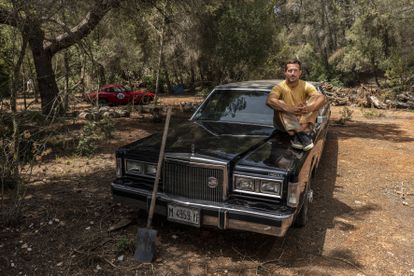 Liam Aldous, director creativo de ColourFeel, en la casa que está restaurando con otras personas en el interior de la isla de Ibiza. En la foto posa con uno de los coches antiguos que tienen en el terreno. 
