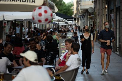 Dos personas pasean por una calle llena de terrazas en el barrio barcelonés del Poblesec