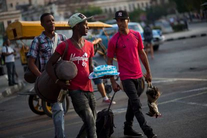 Jóvenes cubanos llevan un tambor, una botella de ron, un pastel y un gallo por una calle de La Habana Vieja, Febrero 17, 2015. 