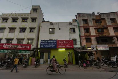 Una mujer cruza en bicicleta delante de los tres bloques de hormigón que conforman el Hospital Medicare de Pune.