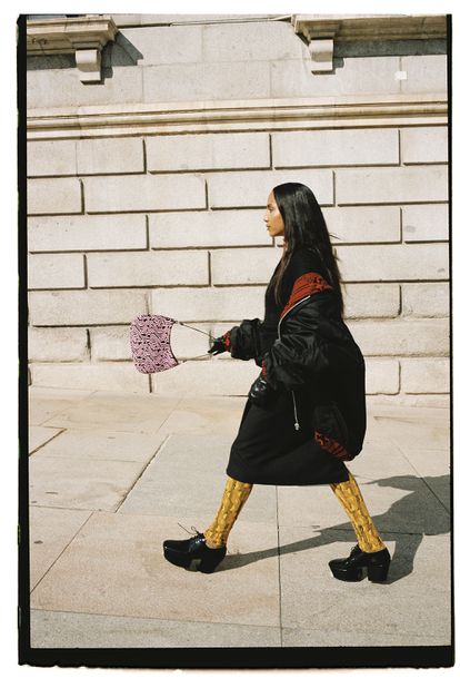 Aquí con bomber de Re-Nylon, mono largo en lana amarilla, polo en lana, falda a rayas y zapatos en piel cepillada, todo de Prada.