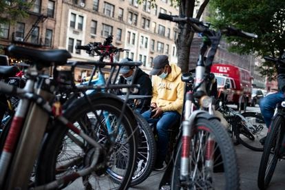 Repartidores de comida a domicilio consultan sus móviles a la espera de un nuevo encargo, en Nueva York.