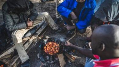Un grupo de inmigrantes cocina y se calienta junto a un fuego en el campamento en el que aguardan para cruzar desde Calais, en Francia, hasta el Reino Unido