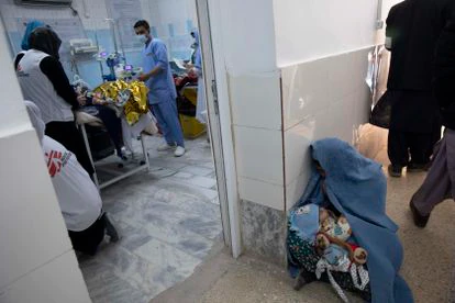 Una mujer afgana espera sentada en el suelo de la clínica de alimentación terapéutica en Herat a que su hijo enfermo sea atendido mientras el personal de Médicos Sin Fronteras trata a otros pacientes.