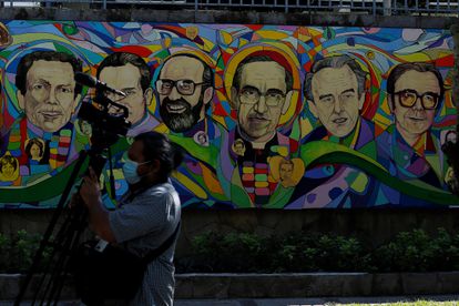 Un camarógrafo camina frente a una pintura dedicada a San Óscar Romero y seis sacerdotes jesuitas asesinados el 16 de noviembre de 1989 en San Salvador.