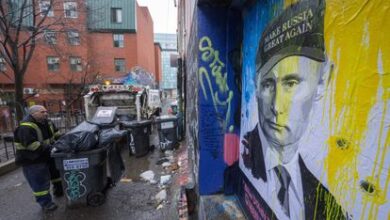Un hombre recoge la basura de un callejón de Toronto ante un retrato de Vladímir Putin, este lunes.