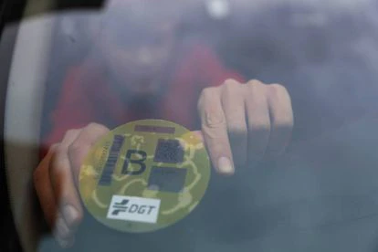 Un hombre coloca la etiqueta ambiental amarilla de la DGT en la luna de su coche.