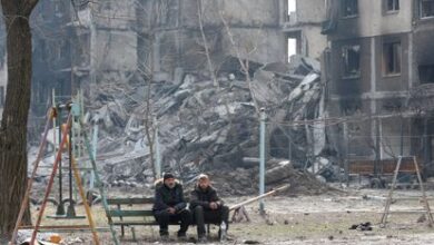 Dos vecinos sentados en un banco delante de edificios destruidos por los bombardeos en Mariupol, el 25 de marzo.