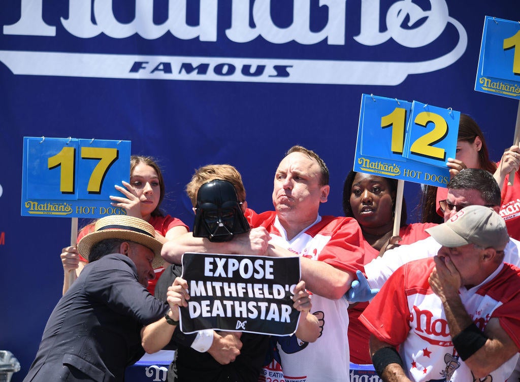 Joey Chestnut derriba a un manifestante en camino a ganar el 15º concurso de comer perritos calientes
