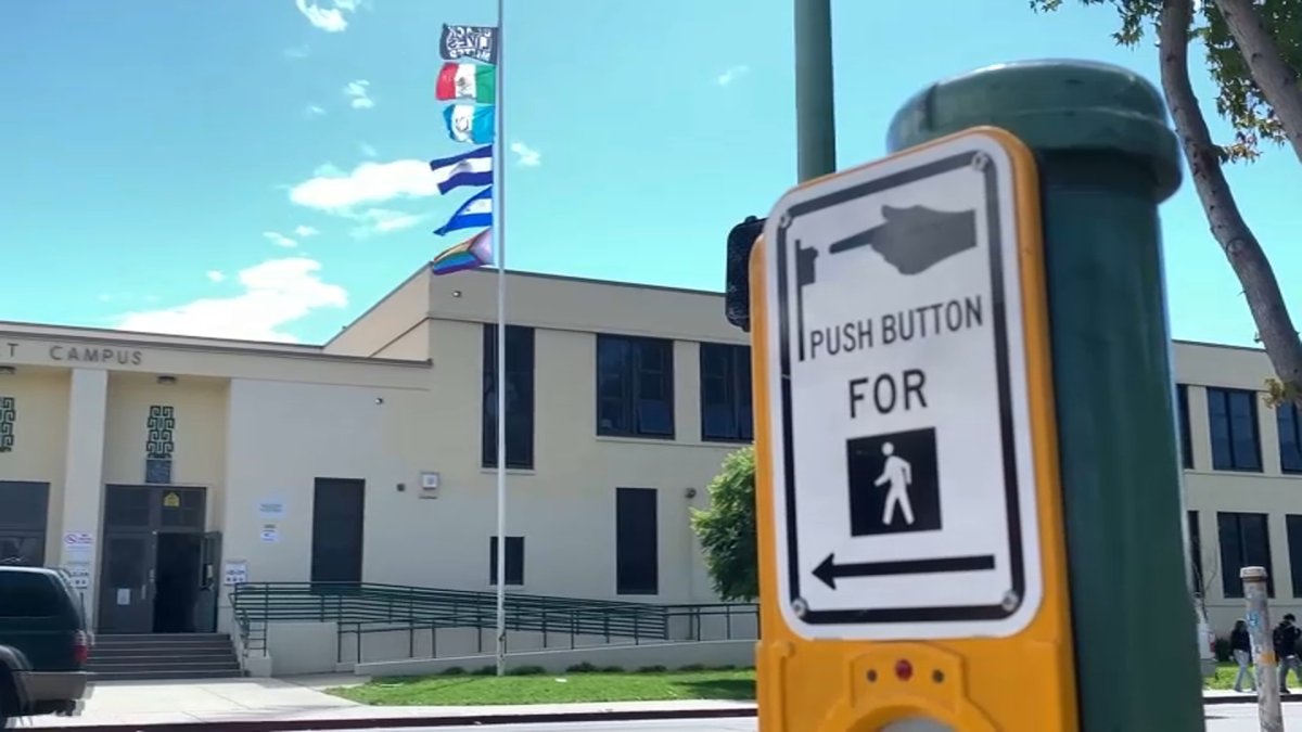mujer baja del asta banderas de países latinos izadas en una escuela en Oakland