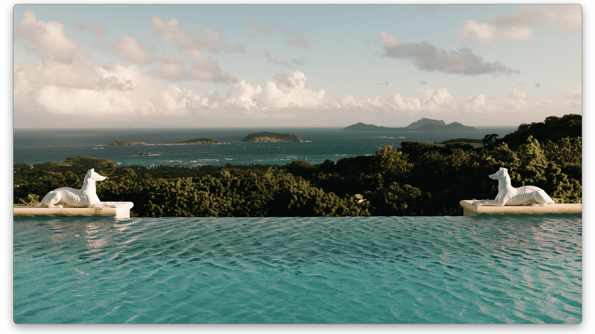 The main home's infinity-edged pool appears to spill into the estate's lush green landscape.