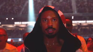 Michael B. Jordan in Creed 3 walking into the boxing ring in a robe flooded with red light surrounded by a cheering crowd