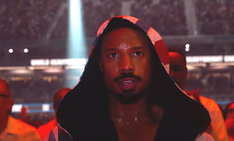 Michael B. Jordan in Creed 3 walking into the boxing ring in a robe flooded with red light surrounded by a cheering crowd