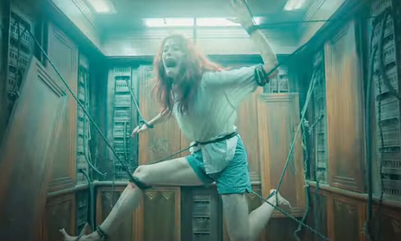 Alyssa Sutherland as Ellie in Evil Dead Rise in an elevator screaming with terror as ropes hold her in an unnatural position