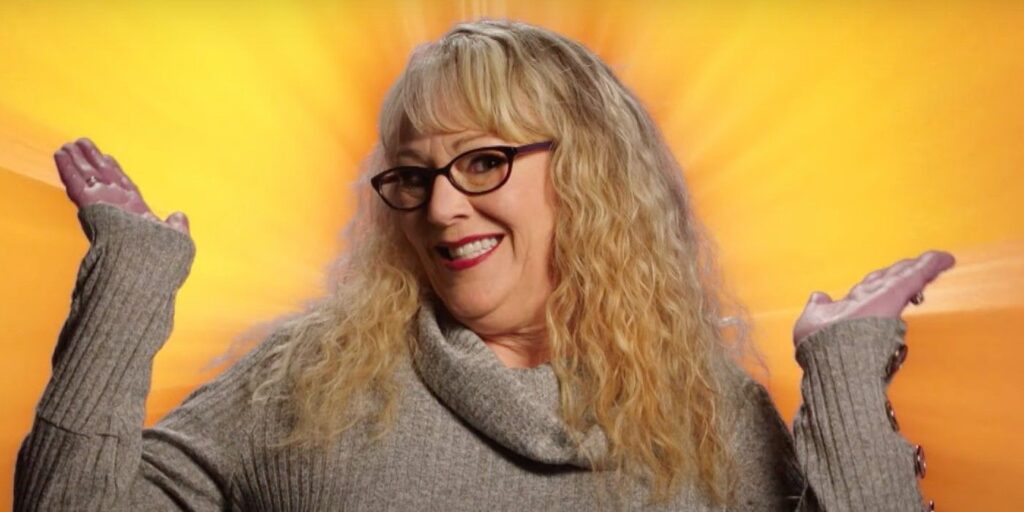 Michelle Rider from The Circle smiling and raising hands up in front of yellow background