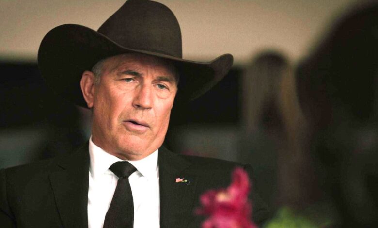 Kevin Costner in Yellowstone in a black cowboy hat at a formal occasional, having a conversation at a table