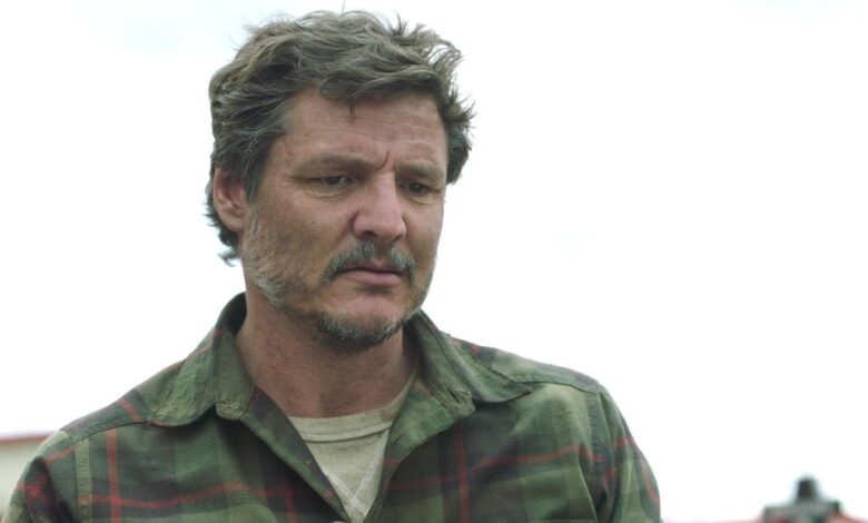 Pedro Pascal as Joel in The Last of Us gazing down with a somber expression on his face, a gray sky in the background