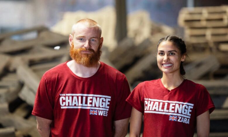 Zara Zoffany standing beside Wes Bergmann on The Challenge: World Championship. They are wearing red shirts with The Challenge logo and the UK flag. They are standing against a backdrop of debri in a warehouse.