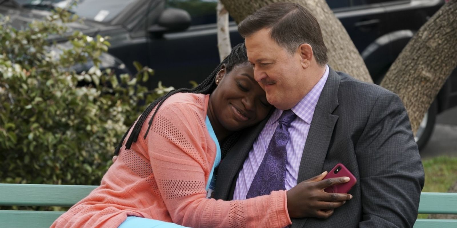 Bob and Abishola embrace one another while sitting outside on a bench in Bob Hearts Abishola