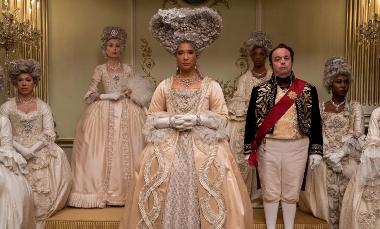 Queen Charlotte in Queen Charlotte: A Bridgerton Story at court surrounded by women in white dresses with a male court servant next to her.