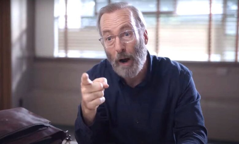 Bob Odenkirk in Lucky Hank wearing a thick beard and glasses, pointing angrily at someone during a meeting