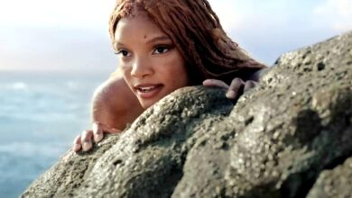Halle Bailey as Ariel hiding behind a rock in The Little Mermaid